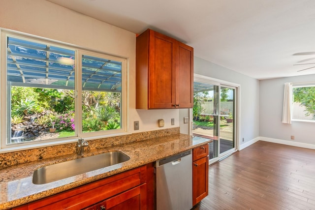 kitchen featuring dark wood finished floors, a sink, light stone countertops, dishwasher, and baseboards