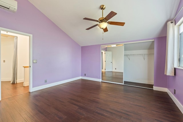 unfurnished bedroom with a wall unit AC, baseboards, vaulted ceiling, and wood finished floors