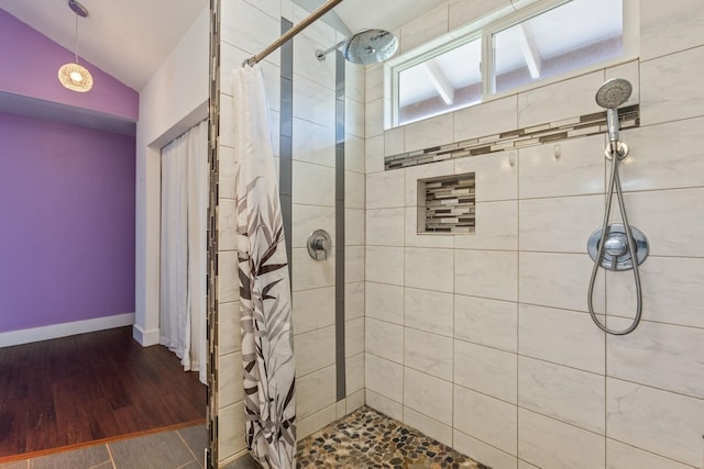 bathroom featuring lofted ceiling, tiled shower, baseboards, and wood finished floors