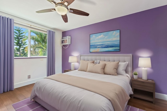 bedroom with a ceiling fan, a wall mounted air conditioner, baseboards, and wood finished floors