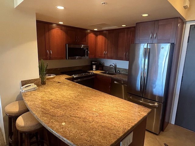 kitchen featuring a kitchen bar, stainless steel appliances, sink, kitchen peninsula, and light stone counters