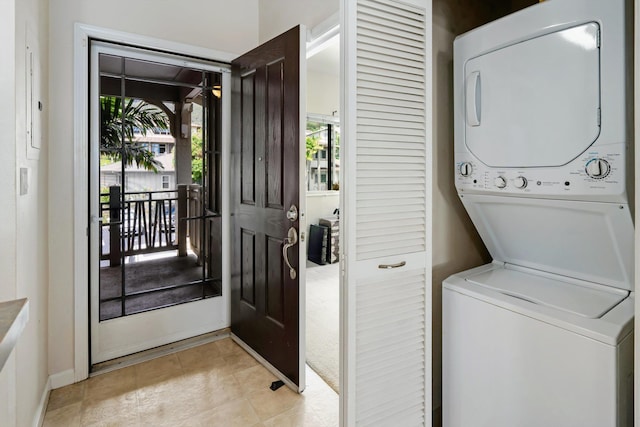 washroom featuring stacked washer and dryer, laundry area, light tile patterned floors, and baseboards