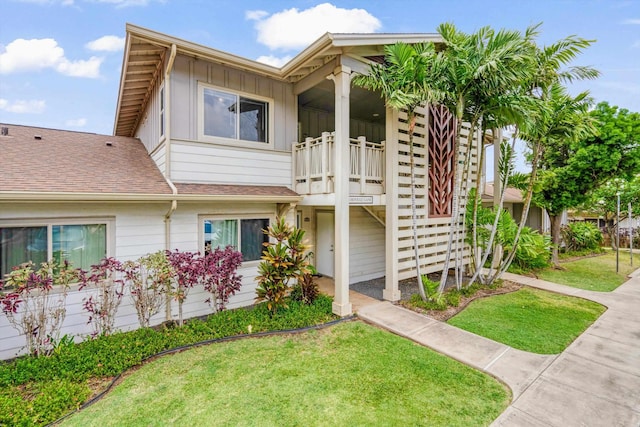 multi unit property featuring a shingled roof, board and batten siding, a balcony, and a front yard