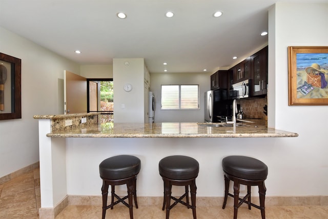 kitchen featuring a peninsula, light stone countertops, stainless steel microwave, and freestanding refrigerator