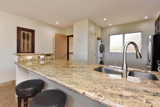 kitchen with kitchen peninsula, stainless steel refrigerator, light stone countertops, light tile patterned floors, and sink