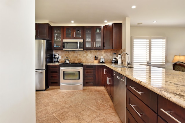 kitchen featuring appliances with stainless steel finishes, backsplash, light stone counters, light tile patterned floors, and sink