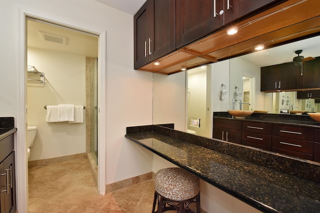 kitchen with dark brown cabinetry, dark stone counters, a kitchen breakfast bar, and light tile patterned floors