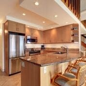 kitchen featuring appliances with stainless steel finishes, light tile patterned flooring, a breakfast bar, a tray ceiling, and sink