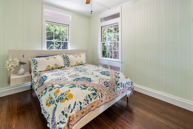 bedroom featuring ceiling fan, wood walls, and dark wood-type flooring