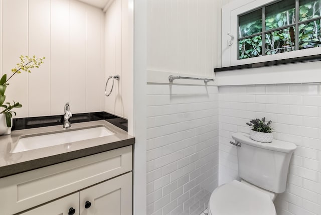 bathroom featuring vanity, toilet, and tile walls