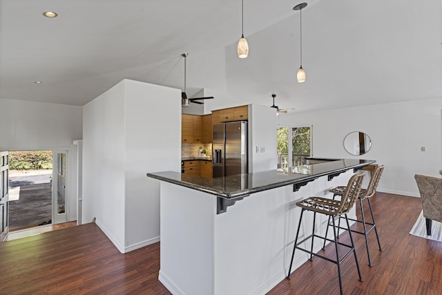 kitchen featuring dark wood-style floors, stainless steel refrigerator with ice dispenser, dark countertops, a kitchen breakfast bar, and brown cabinets