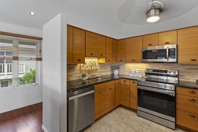 kitchen with a sink, stainless steel appliances, dark stone countertops, and decorative backsplash