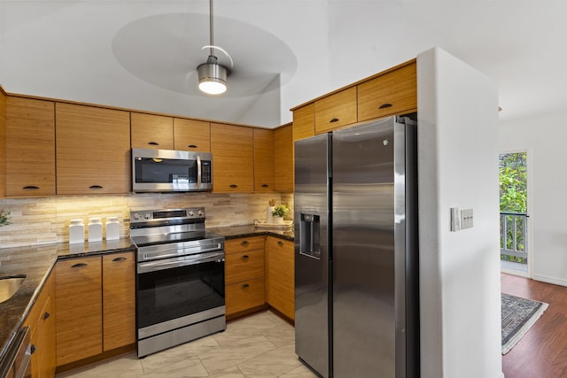 kitchen with decorative backsplash, dark stone countertops, brown cabinetry, and stainless steel appliances