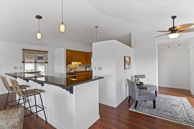 kitchen with dark countertops, backsplash, dark wood-type flooring, a kitchen bar, and brown cabinets