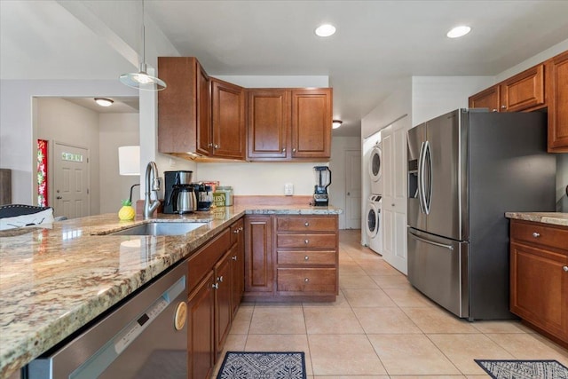 kitchen with hanging light fixtures, sink, stacked washer and dryer, light tile patterned floors, and appliances with stainless steel finishes