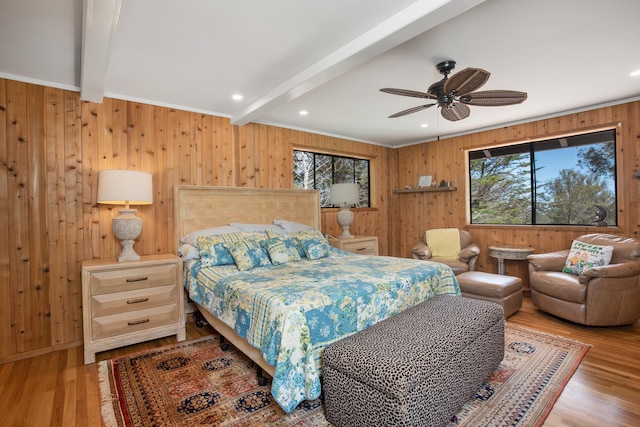 bedroom with beam ceiling, wooden walls, a ceiling fan, and wood finished floors