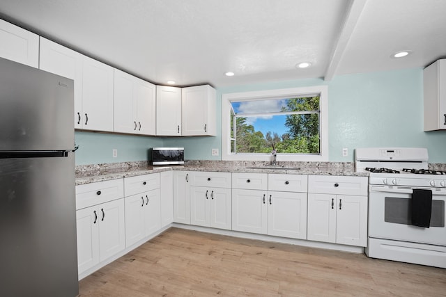 kitchen with a sink, light stone countertops, appliances with stainless steel finishes, and light wood finished floors