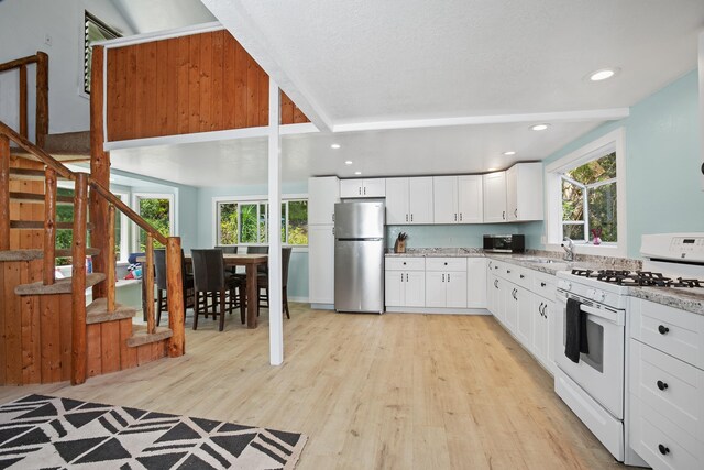 kitchen featuring white range with gas cooktop, white cabinets, light wood-type flooring, and freestanding refrigerator