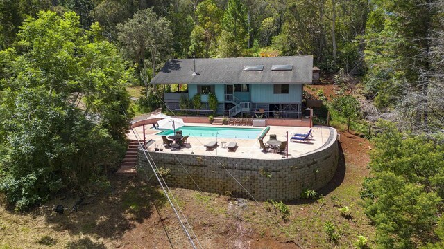 outdoor pool with a forest view, a patio, and stairs