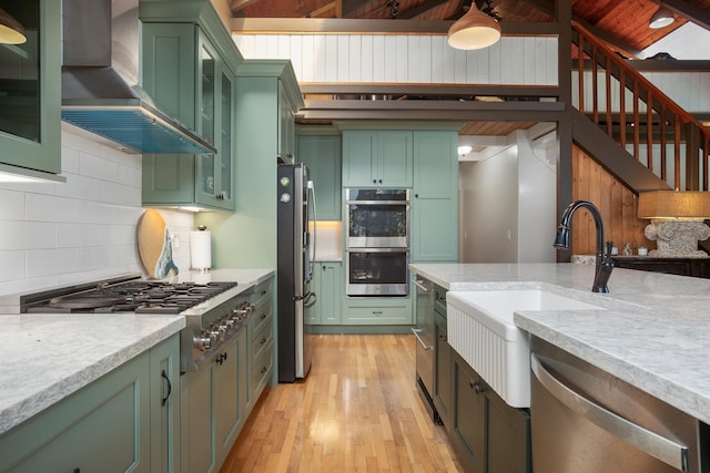 kitchen featuring green cabinets, wall chimney range hood, and stainless steel appliances