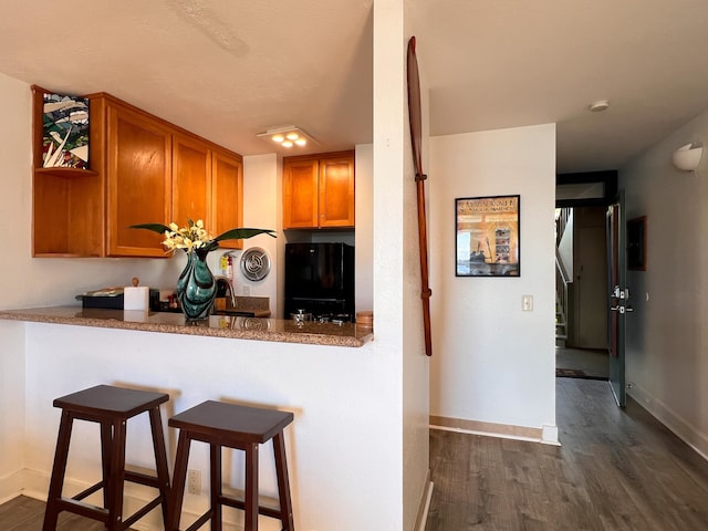 kitchen featuring black refrigerator, dark hardwood / wood-style flooring, a kitchen bar, and kitchen peninsula