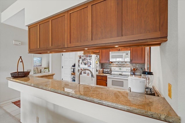 kitchen featuring white appliances, light stone countertops, kitchen peninsula, and backsplash