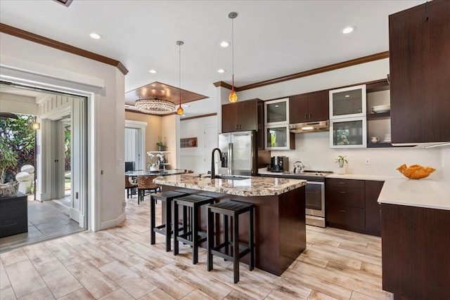 kitchen with appliances with stainless steel finishes, ornamental molding, a center island with sink, and decorative light fixtures