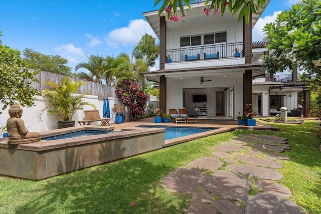 rear view of property featuring a pool with hot tub, a lawn, ceiling fan, a patio area, and a balcony