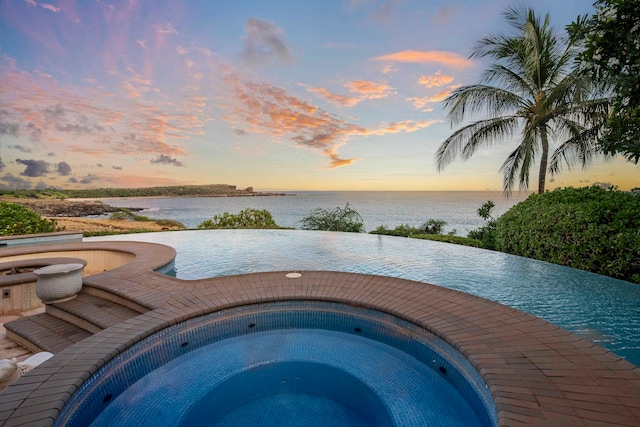 pool at dusk with an in ground hot tub and a water view