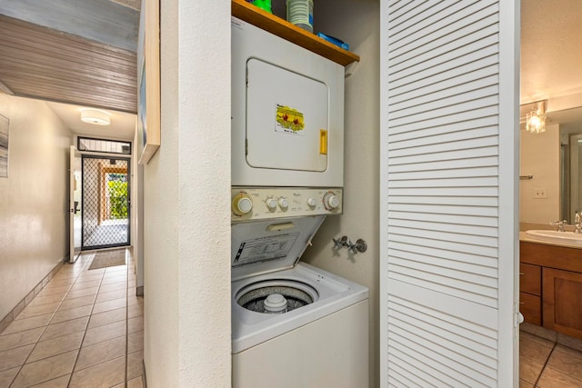 clothes washing area featuring sink, light tile patterned flooring, and stacked washing maching and dryer