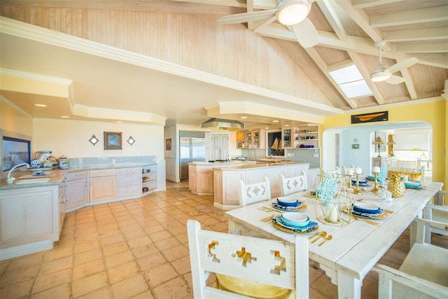 dining area featuring sink, ceiling fan, beam ceiling, a skylight, and high vaulted ceiling