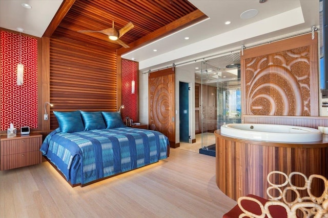 bedroom with light hardwood / wood-style flooring, a tray ceiling, a barn door, wooden ceiling, and wooden walls