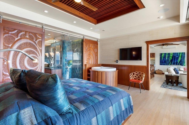 bedroom with a tray ceiling, a barn door, wood ceiling, light hardwood / wood-style floors, and wooden walls