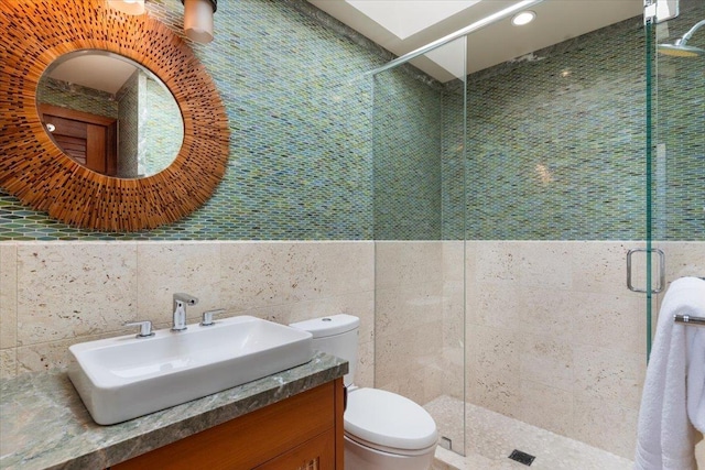 bathroom featuring vanity, toilet, tile walls, and a shower with door