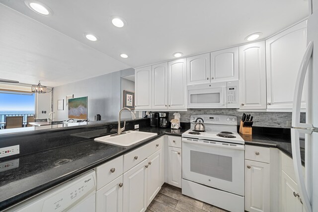 kitchen with dark countertops, white appliances, white cabinetry, and a sink