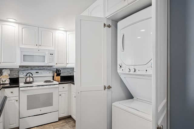 kitchen featuring white appliances, white cabinetry, stacked washing maching and dryer, light wood finished floors, and dark countertops