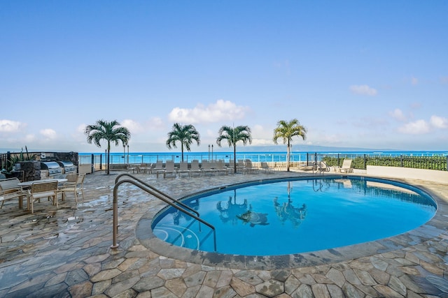 pool featuring a patio, a water view, and fence