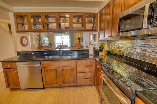 kitchen featuring appliances with stainless steel finishes, tasteful backsplash, sink, dark stone countertops, and light hardwood / wood-style floors