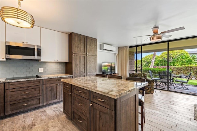2387 S Kihei Rd Unit C108, Kihei, HI 96753 - kitchen with stainless steel microwave, a wall mounted air conditioner, black electric stovetop, white cabinets, and light wood-type flooring