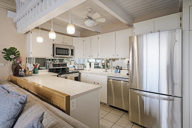 kitchen featuring stainless steel appliances, light tile patterned floors, beam ceiling, decorative light fixtures, and white cabinets