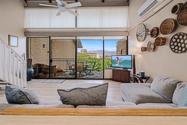 living room featuring hardwood / wood-style flooring, ceiling fan, a towering ceiling, and a wall mounted AC