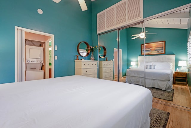 bedroom with vaulted ceiling, ceiling fan, wood-type flooring, stacked washer and clothes dryer, and a closet