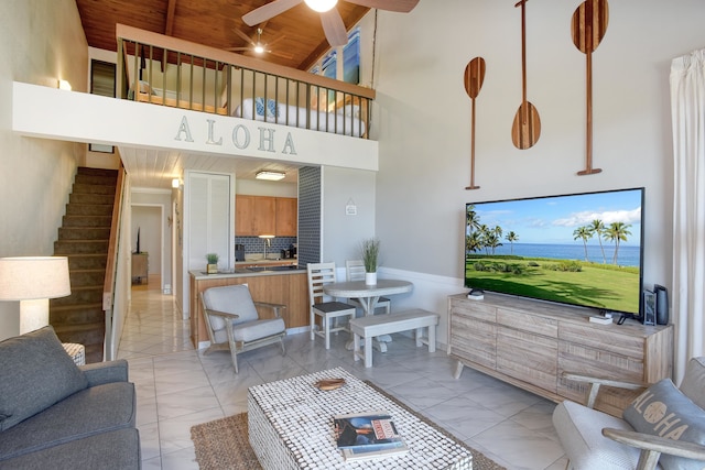 living room featuring beamed ceiling, ceiling fan, wooden ceiling, and a high ceiling