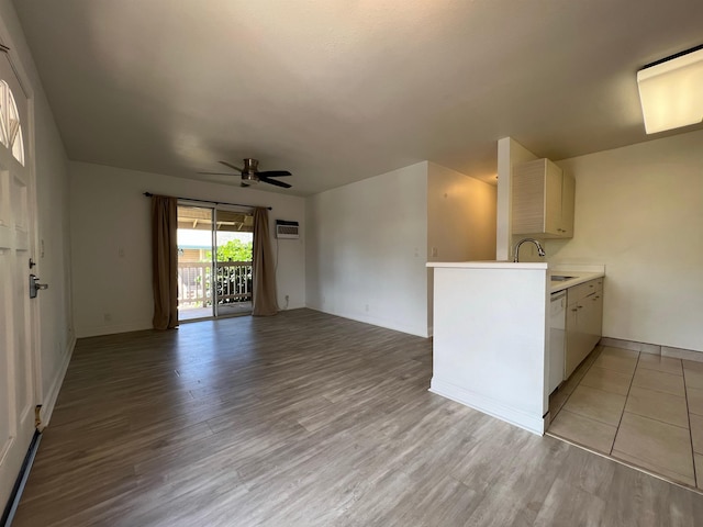 interior space with ceiling fan, an AC wall unit, sink, and light wood-type flooring