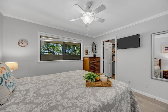 bedroom with baseboards, ornamental molding, ceiling fan, a walk in closet, and wood finished floors