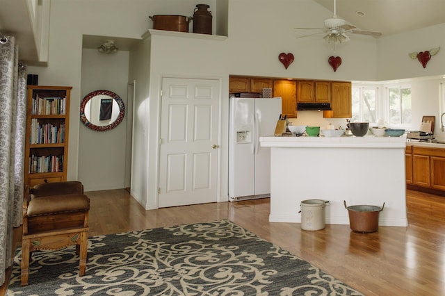 kitchen with a ceiling fan, tile counters, white fridge with ice dispenser, a towering ceiling, and under cabinet range hood