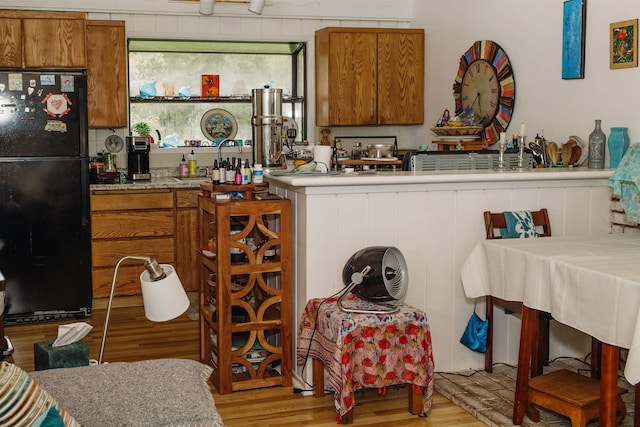 kitchen with brown cabinets, wood finished floors, and freestanding refrigerator