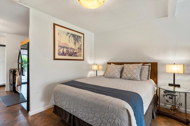 bedroom with black fridge, dark tile flooring, and a textured ceiling