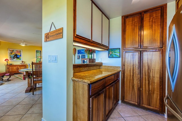 kitchen featuring a ceiling fan, freestanding refrigerator, light stone counters, and light tile patterned floors