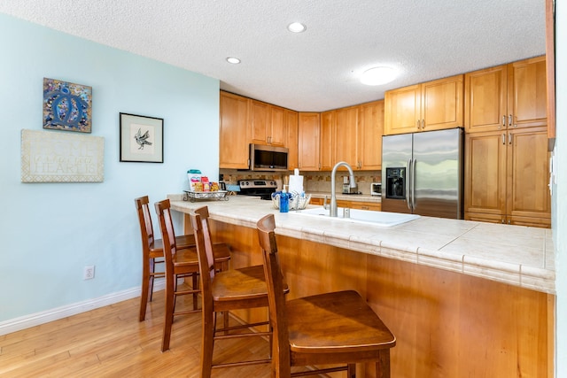 kitchen with tile countertops, a breakfast bar, a textured ceiling, appliances with stainless steel finishes, and kitchen peninsula